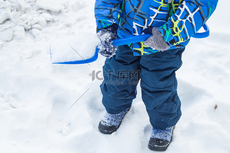 迷人的小男孩在冬日挖雪蓝色小铲