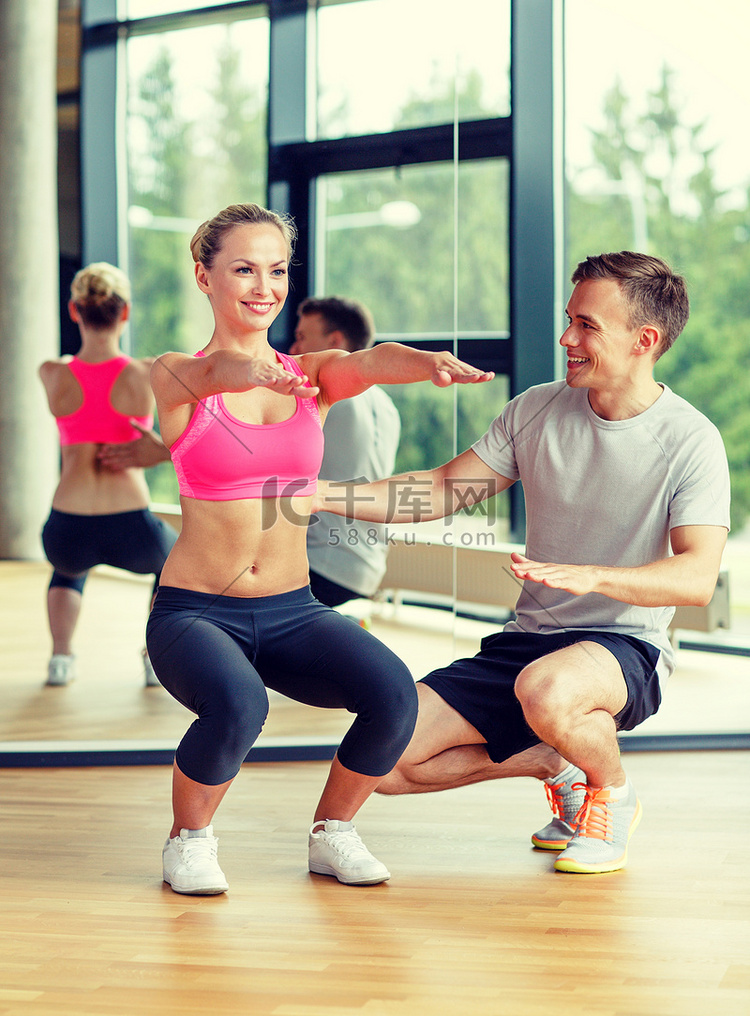 微笑的女人和男教练在健身房锻炼