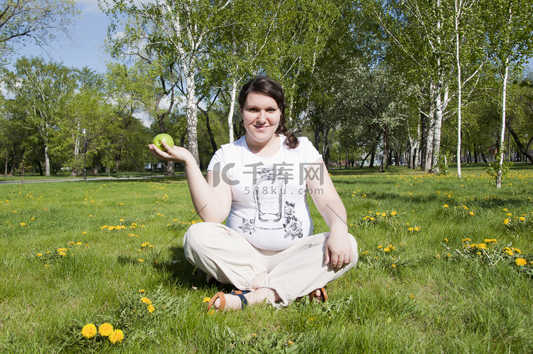 拿着苹果坐在草地上的女人