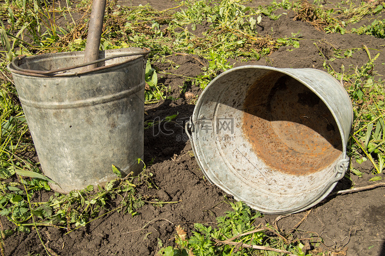花园土草背景下两个旧脏锈铁桶的