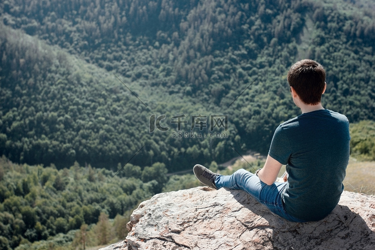夏天，男人坐在岩石上，背景是绿