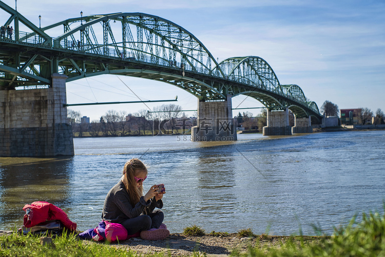 一个小女孩拿着电话坐在河边。