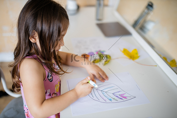 小女孩用笔在纸上给大叶子图像上