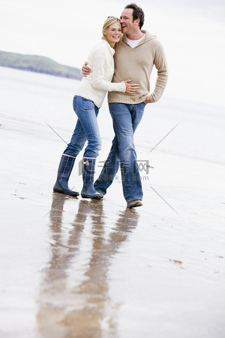 情侣手挽手微笑地走在沙滩上