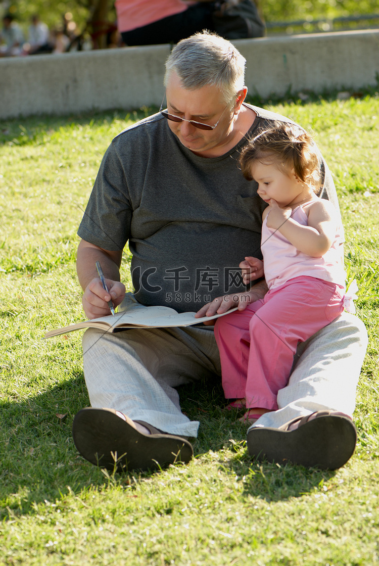 祖父带着孙女坐在公园的草地上