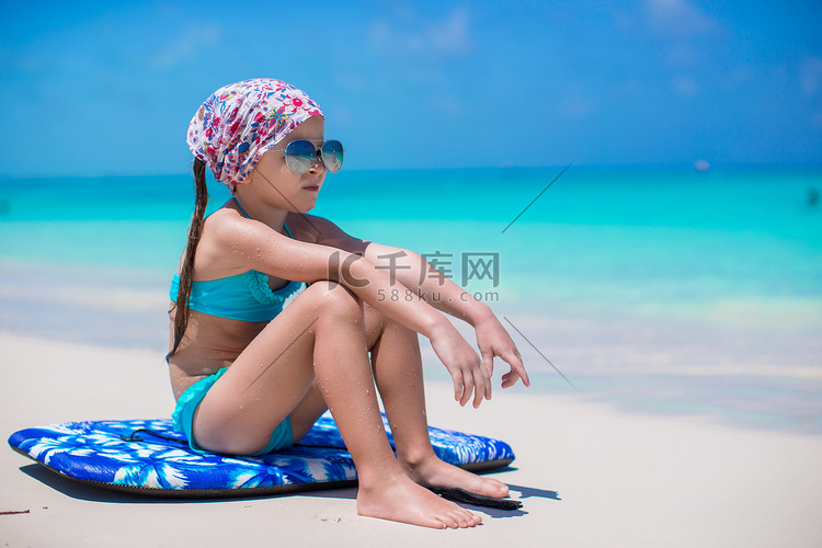 可爱的小女孩坐在海边的冲浪板上