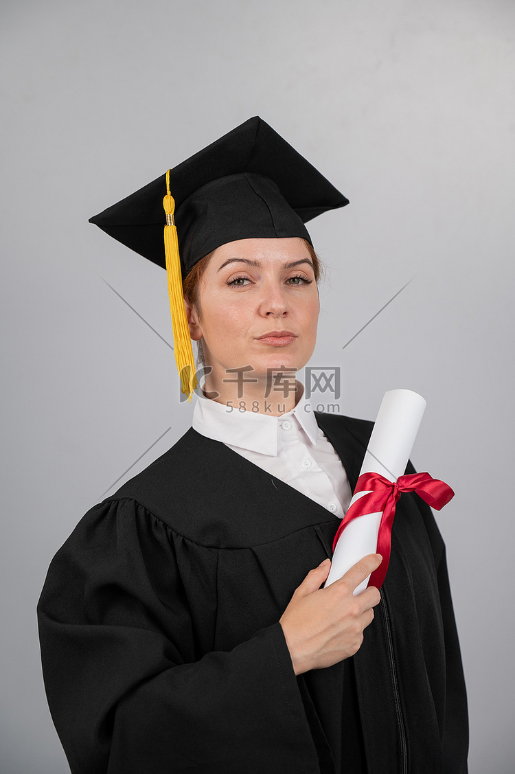 毕业礼服的严肃的妇女拿着在白色