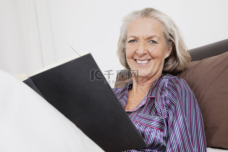 坐在家里拿着书的快乐老年妇女的