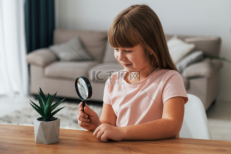 小女孩坐在桌旁，拿着放大镜