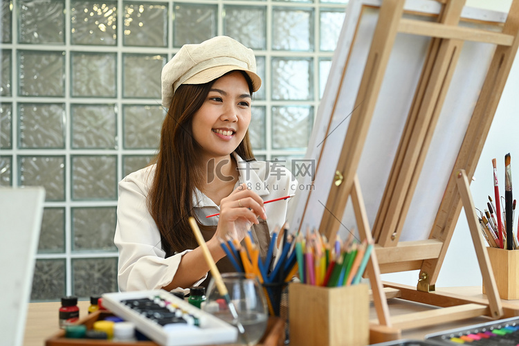 微笑的女画家坐在画布前，用水彩
