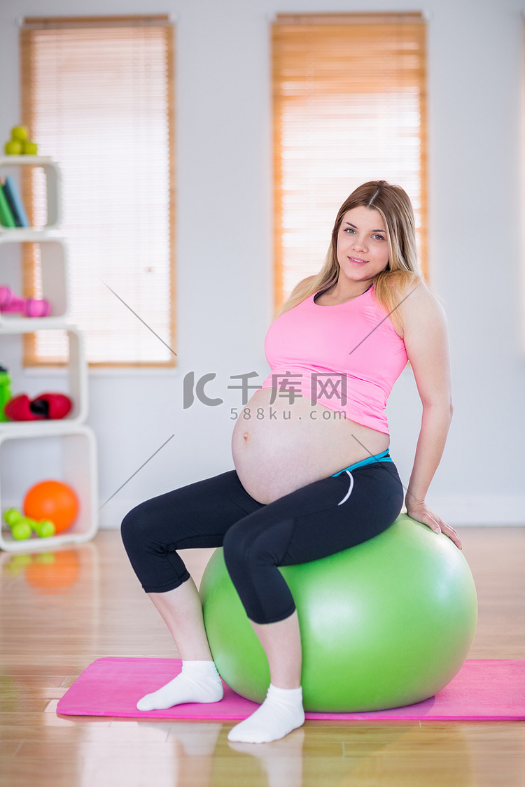 坐在健身球上看着相机的孕妇