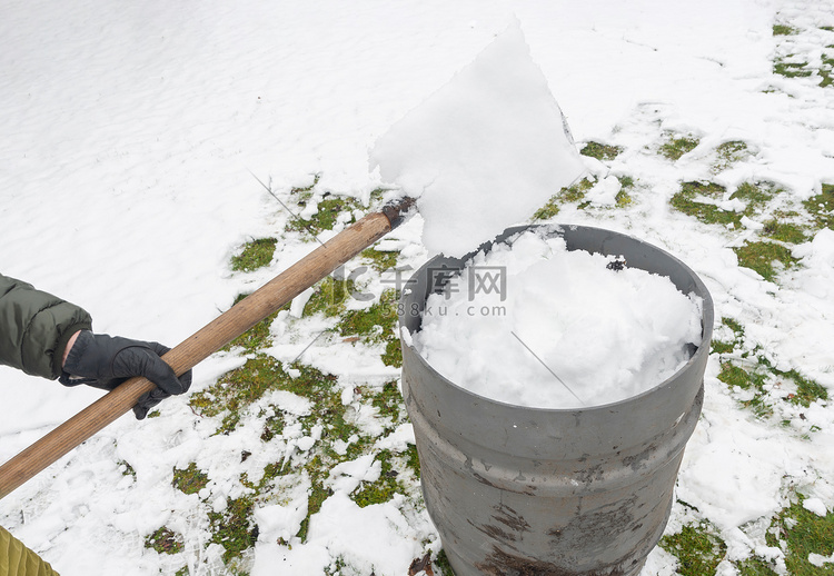 中年妇女正在用铲子在桶里收集雪