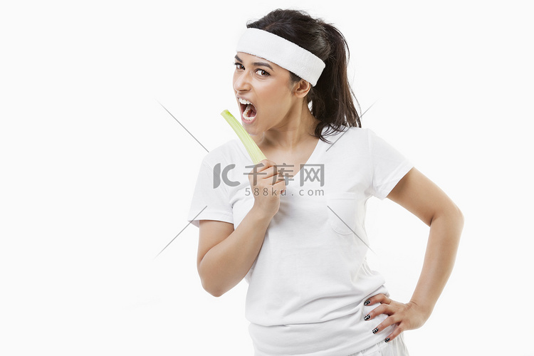 白色背景下吃芹菜的年轻女运动员