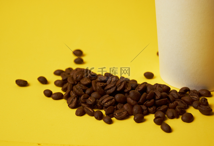 黄色背景中纸杯旁边的咖啡豆