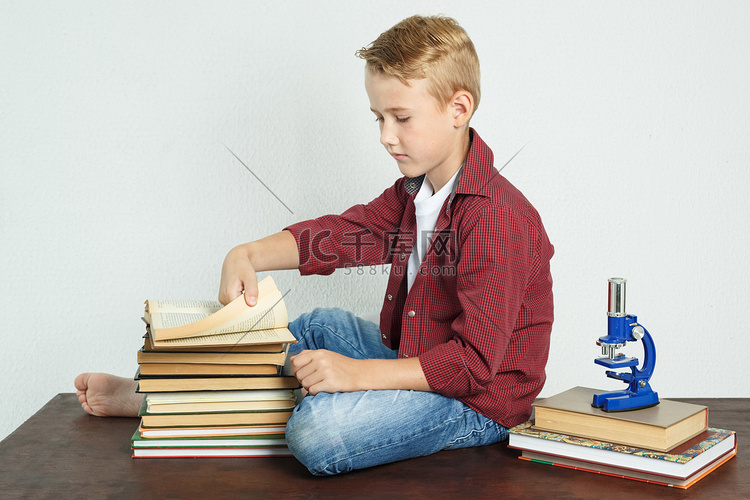 小学生坐在书旁的桌子旁，翻阅着