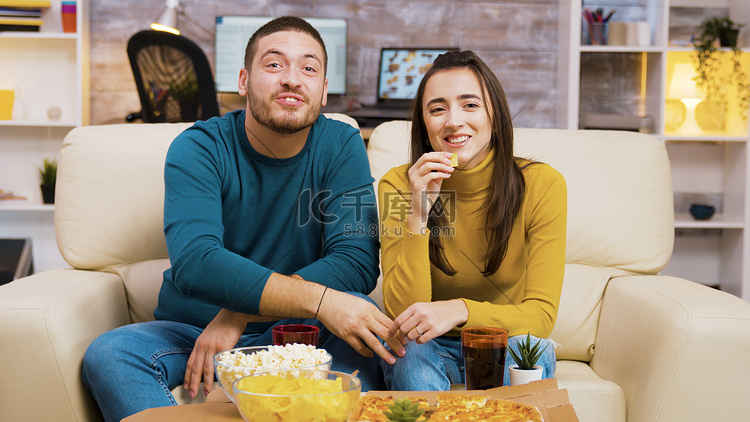 一对夫妇坐在沙发上边看电视边吃