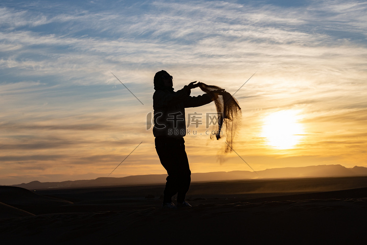 夕阳下在撒哈拉沙漠中跳跃和扔沙