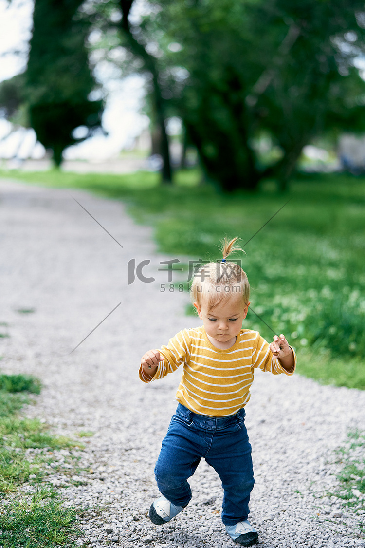 小女孩沿着公园的碎石路走，看着