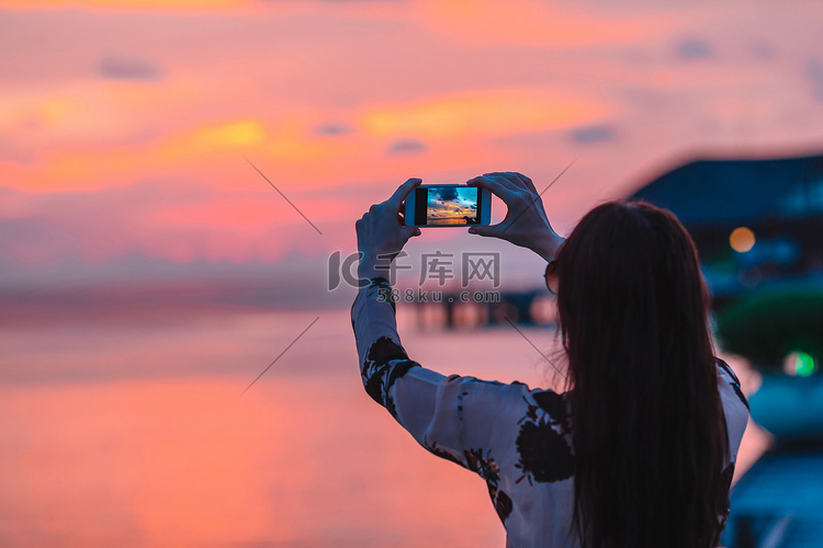 女人在手机上拍美丽日落的照片