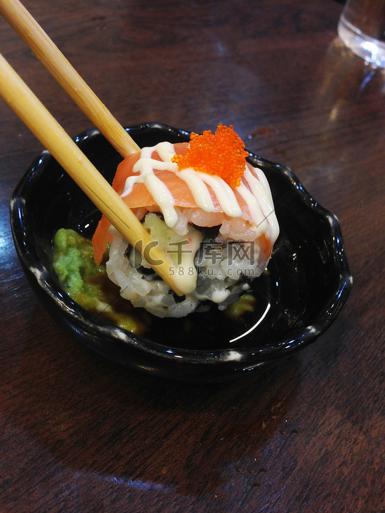 用筷子在酱汁和芥末上夹三文鱼卷