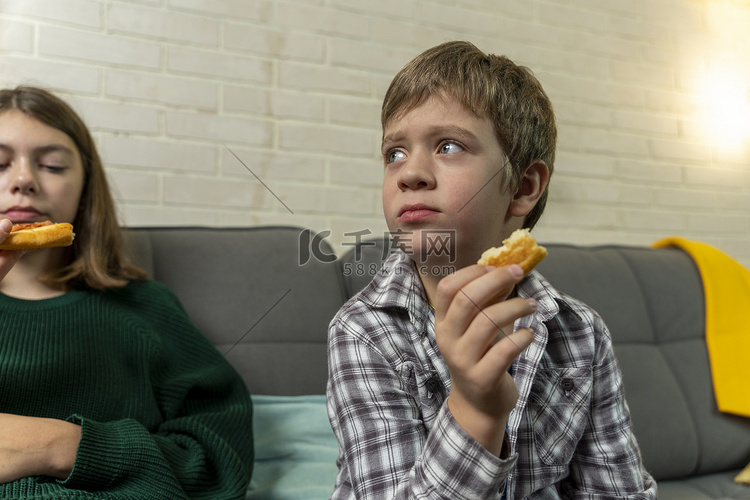 男孩坐在家里的沙发上，吃披萨，
