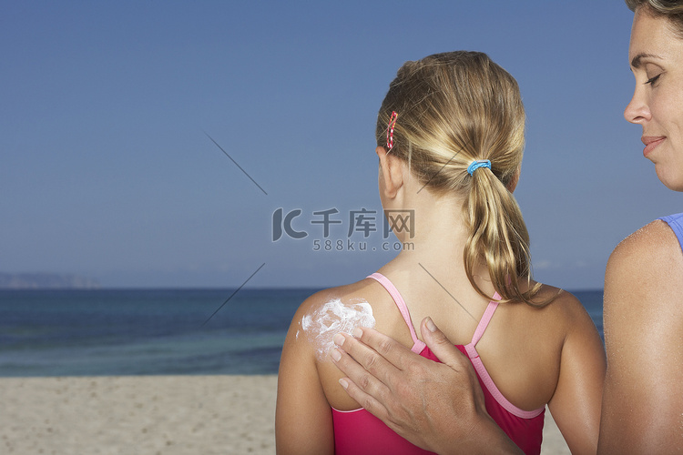 一位短发女性在海滩上给女孩涂防