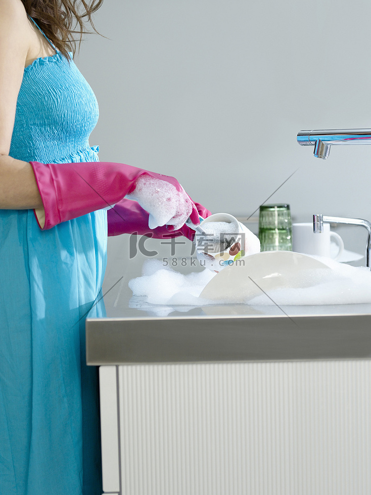 一位身着蓝色裙子和橡胶手套洗碗