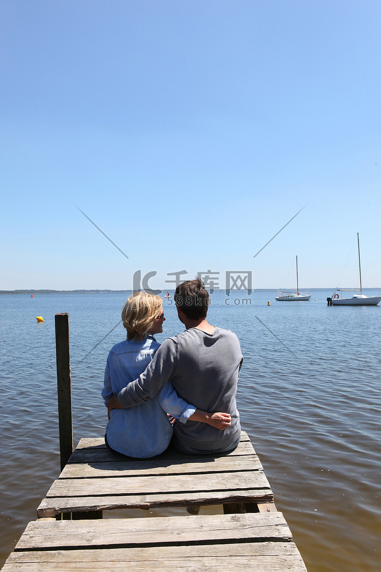 一对夫妇坐在浮桥的尽头，双臂环