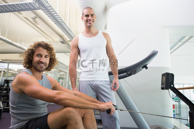 男教练协助男子在健身房使用健身