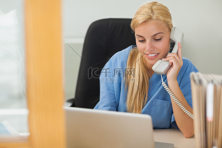 金发护士在笔记本电脑旁边打电话