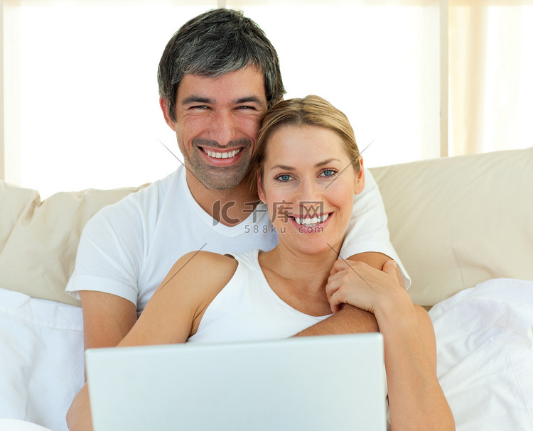 微笑的夫妇躺在床上使用笔记本电
