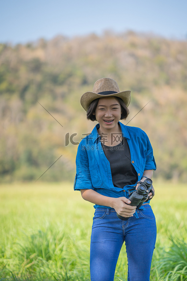 女人戴帽子，在草地上拿着双筒望