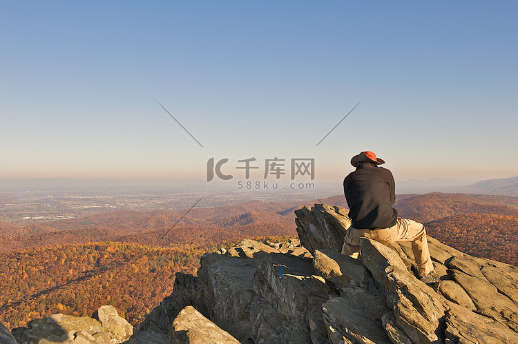 男人坐在一块岩石上，俯瞰着风景