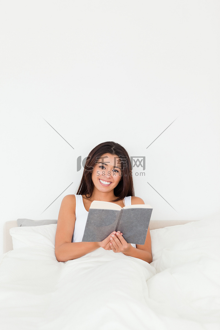 黑发女人拿着书坐在床上看着相机