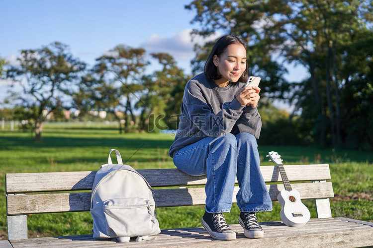 年轻女子坐在公园的长凳上，拿着