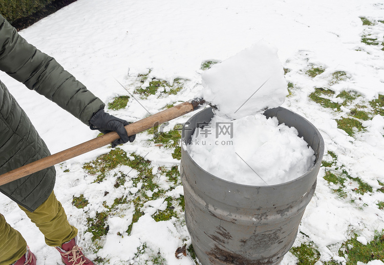 中年妇女正在用铲子在桶里收集雪
