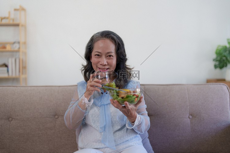 快乐的亚洲老妇人吃新鲜的绿色沙