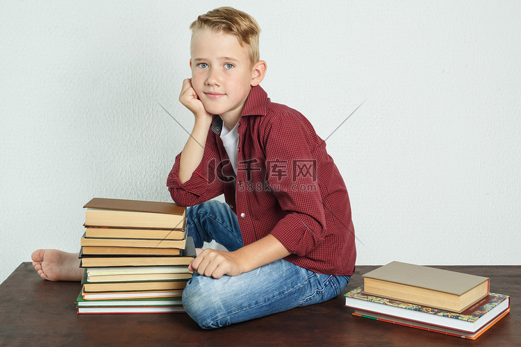 一个男生坐在靠近书本的桌子上，