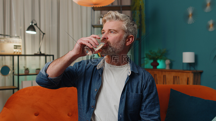 口渴的中年男子坐在家里，手里拿