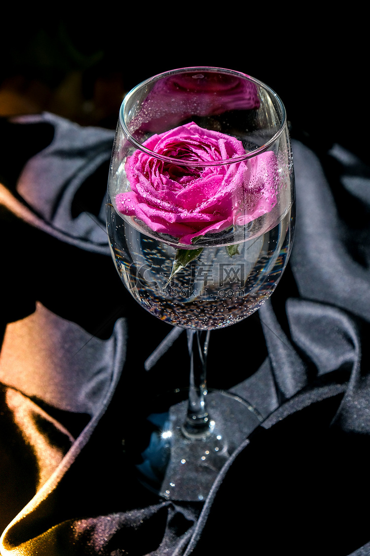 装满粉红色花瓣的酒杯放在黑色丝