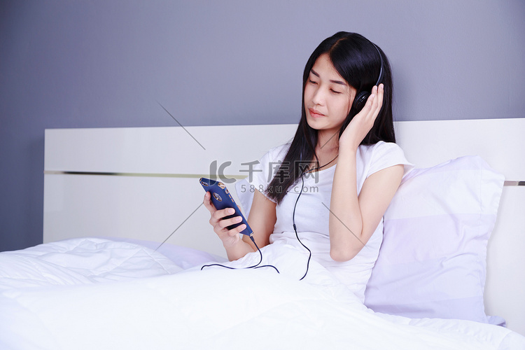 戴耳机的女人在卧室床上用智能手