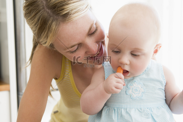 母亲和婴儿在厨房里吃胡萝卜