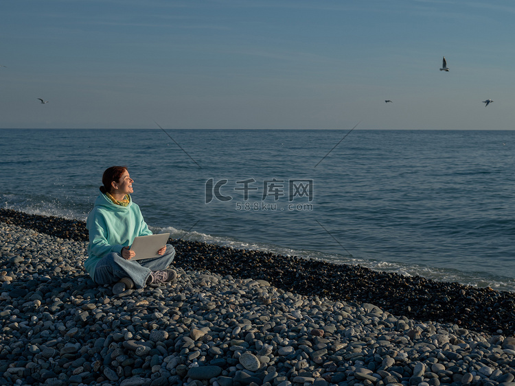快乐的白种女人坐在圆石滩上用笔