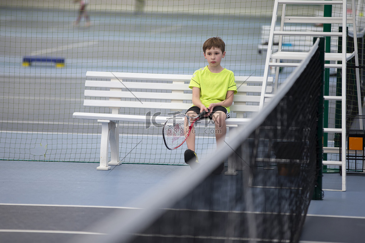 悲伤的男孩坐在网球比赛的长凳上