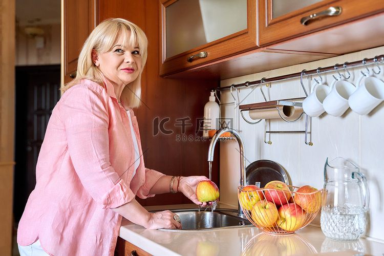 成熟女人在家里的厨房里洗苹果