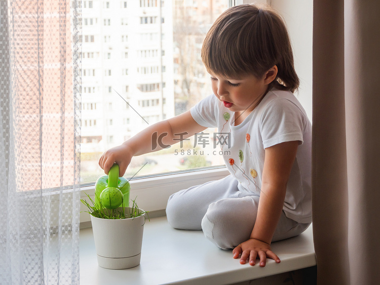 蹒跚学步的男孩坐在窗台上，浇花