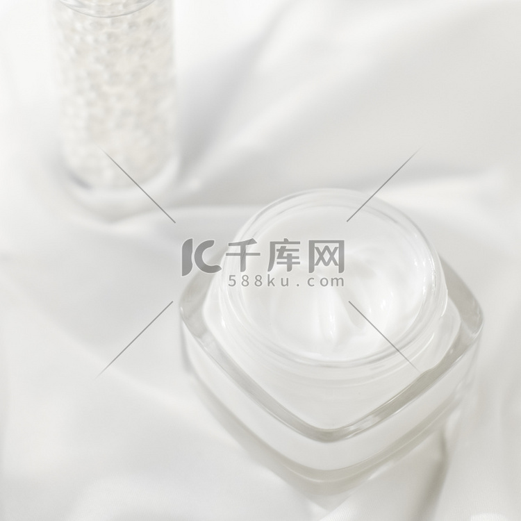 白丝绸上的面霜保湿罐和血清凝胶
