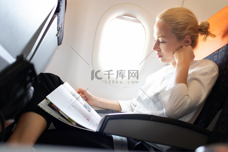 在飞机上阅读飞行杂志的女人。