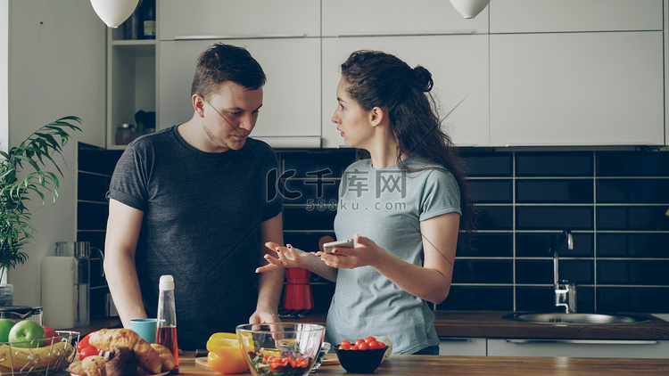 年轻的卷发女人在丈夫做饭时在手