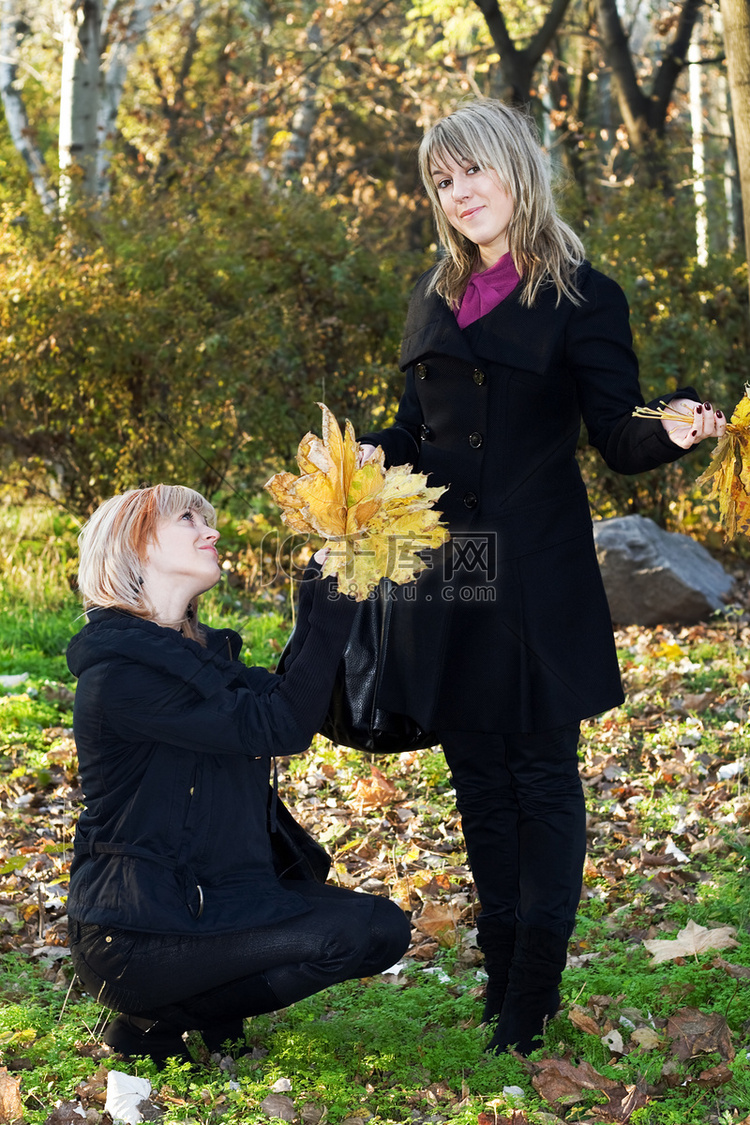 公园里有秋叶的两个漂亮的年轻女